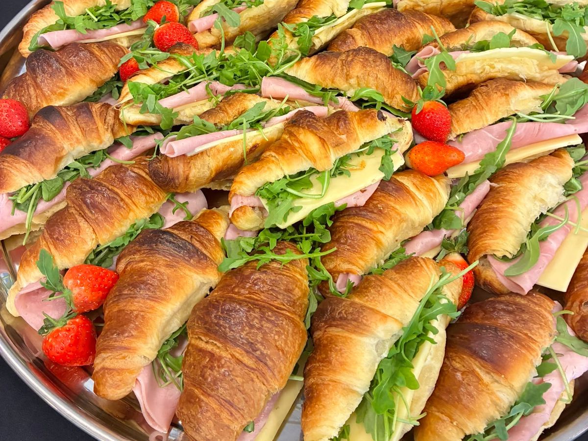 A platter of ham, cheese and rocket croissant sandwiches with strawberries