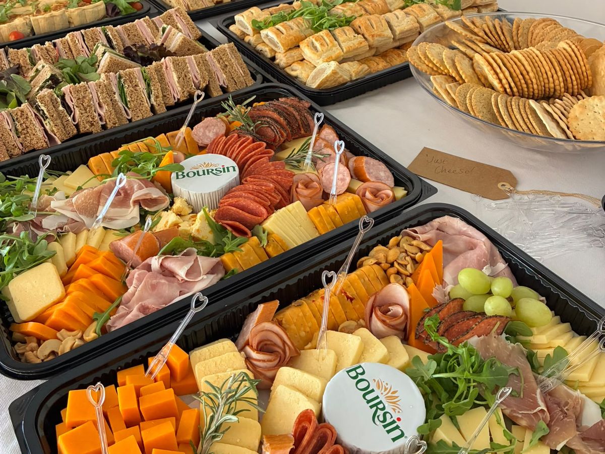 Cheese and charcuterie trays with sandwiches and sausage rolls on a buffet table